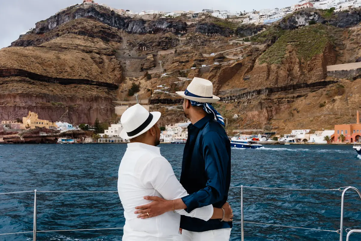 A newly engaged couple embrace aboard a boat with the town of Fira on the cliffs behind