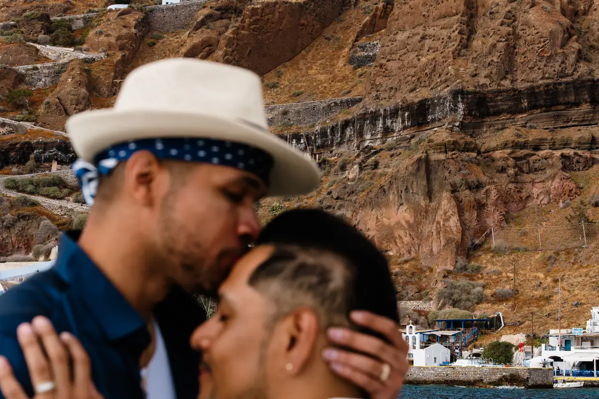 A photographer's candid frame of a couple sharing a forehead kiss beneath the Santorini cliffs