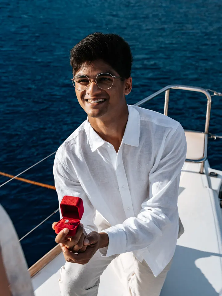A smiling man holds open a red ring box aboard a private yacht on the Aegean Sea
