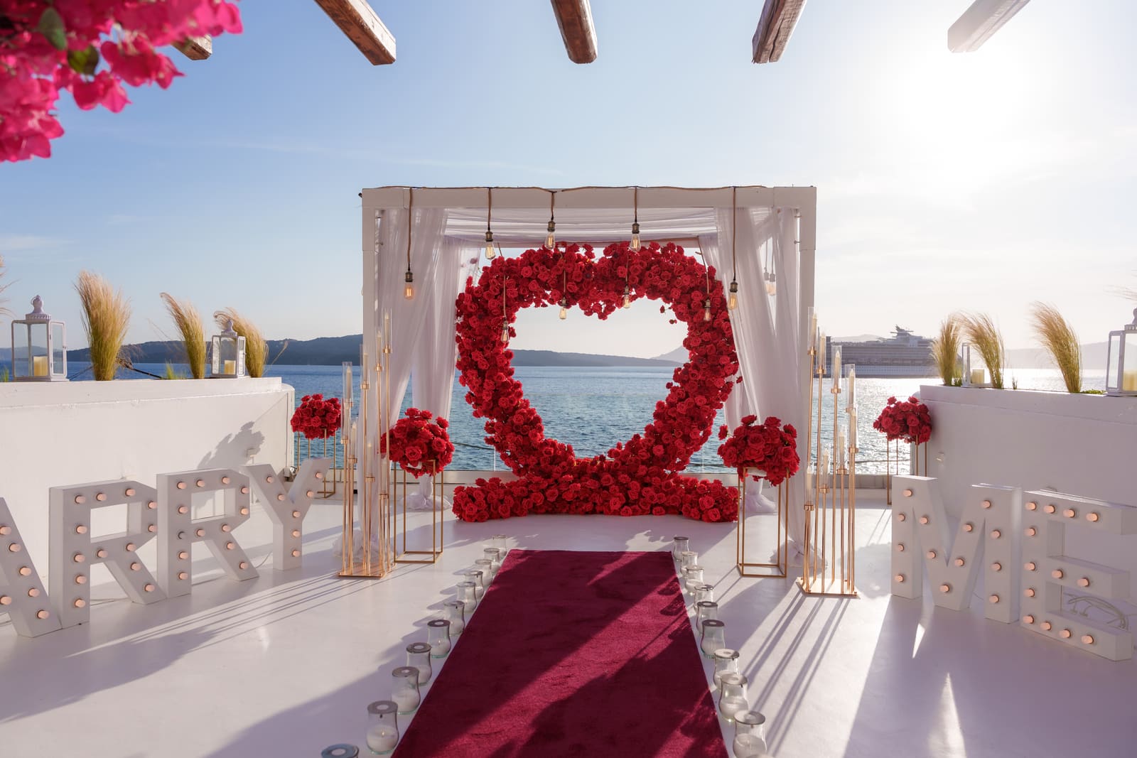 Un arco a forma di cuore di rose rosse che incornicia il Mar Egeo su una terrazza bianca a strapiombo a Santorini