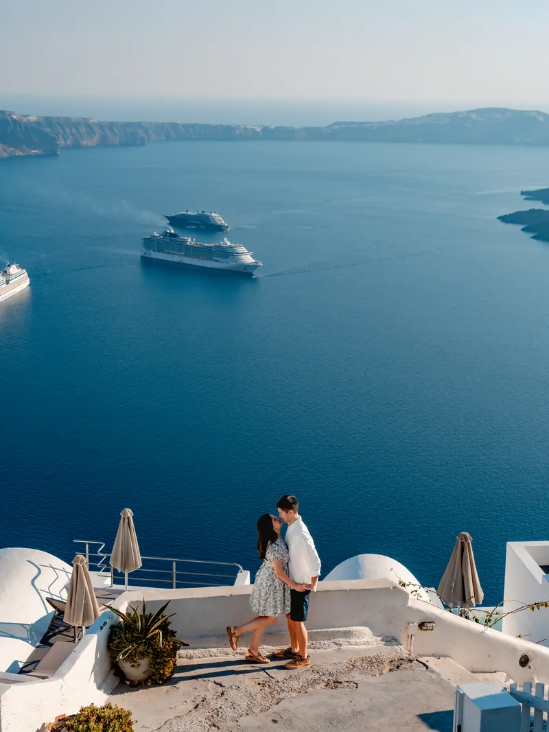 A couple embrace on a white caldera-edge terrace high above the deep blue Aegean in Imerovigli