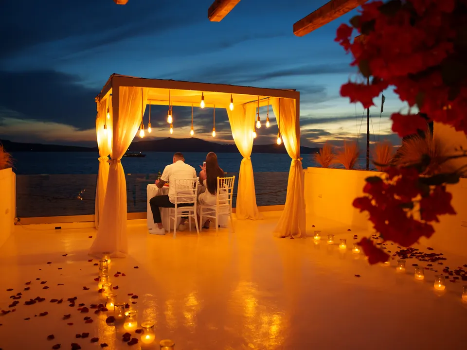 A candlelit private terrace dinner under a draped cabana at dusk overlooking the Aegean Sea in Santorini