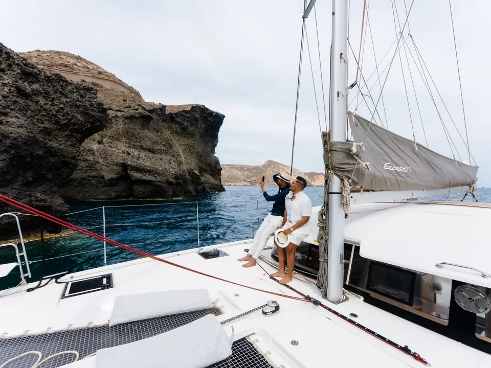 A couple aboard a private catamaran beside the sea cliffs of the Santorini caldera