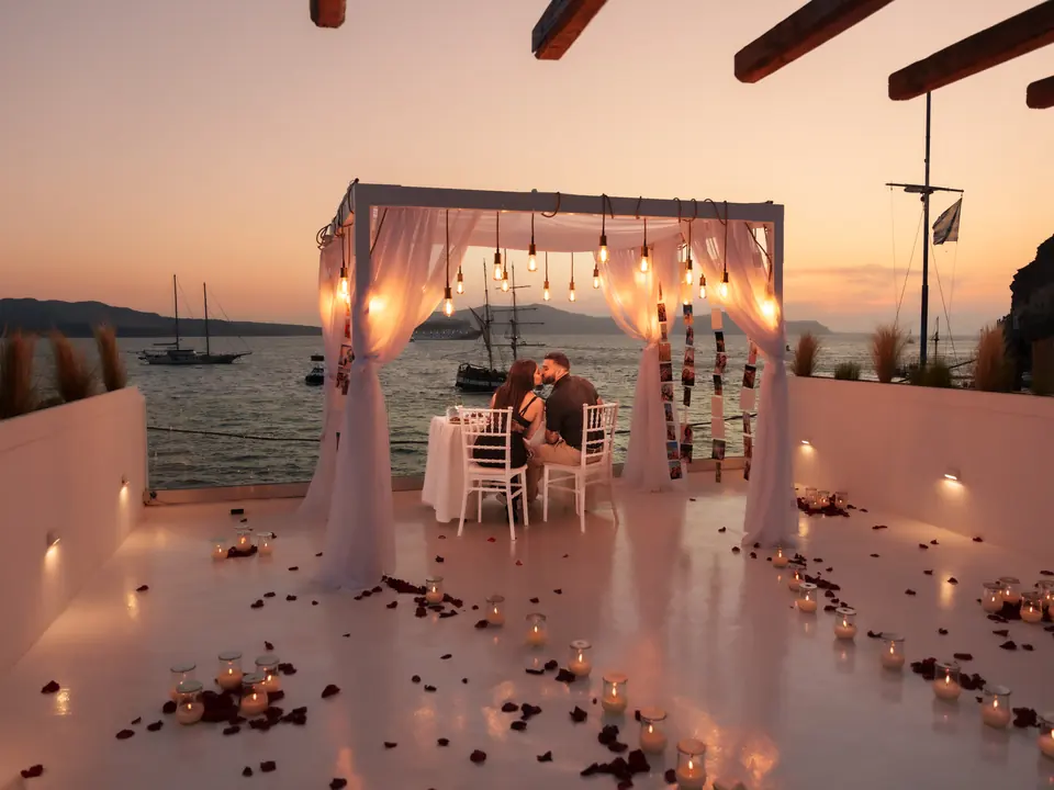 A candlelit draped cabana on a private villa terrace overlooking the Santorini caldera at dusk