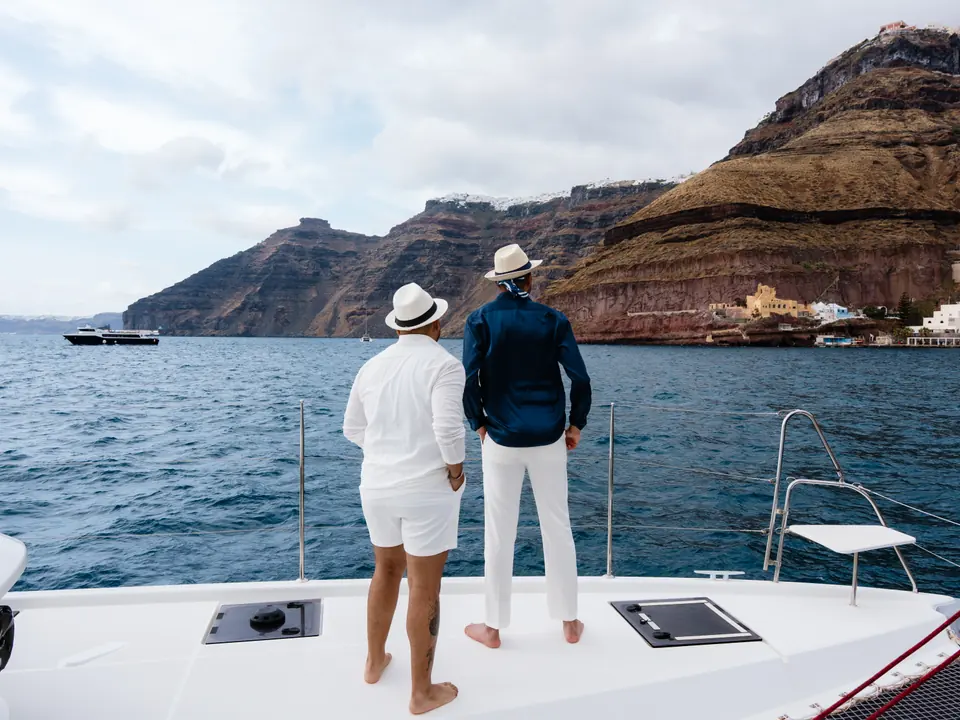 A couple at the bow of a private catamaran gazing toward the cliffs of Fira, Santorini