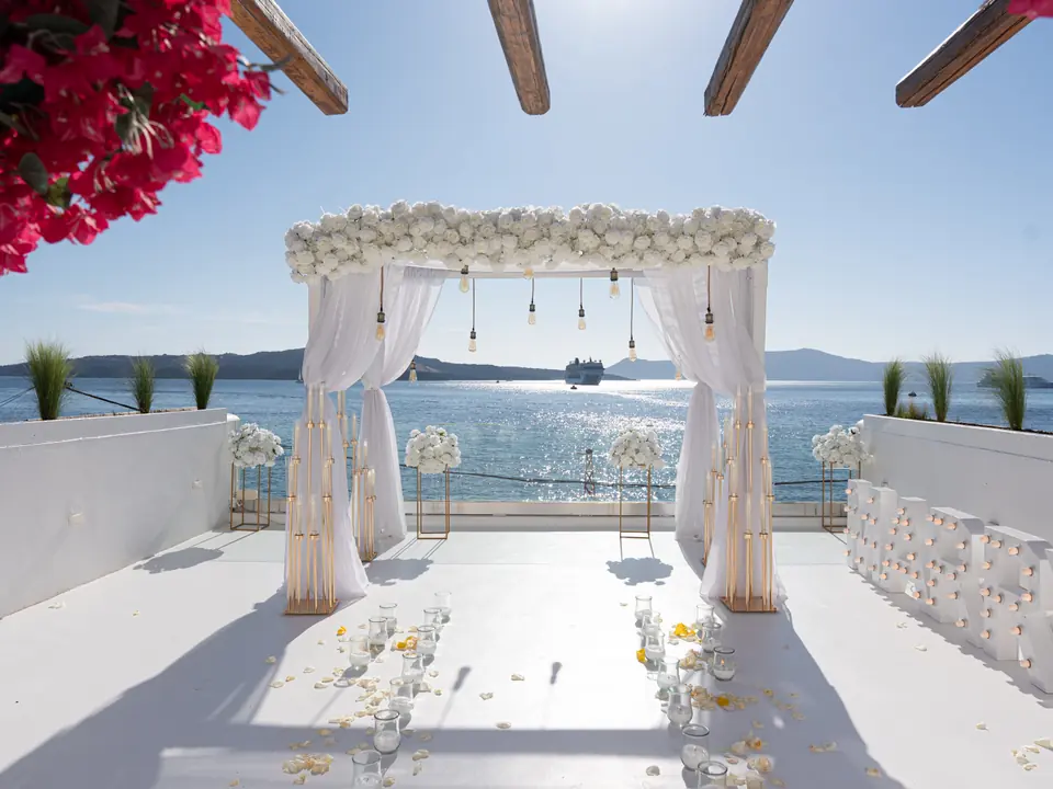 A white floral proposal arch and aisle being styled on a Santorini terrace before the reveal
