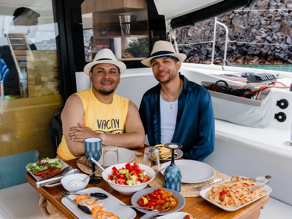 A couple enjoy a private dining spread of fresh dishes and wine aboard a catamaran off Santorini