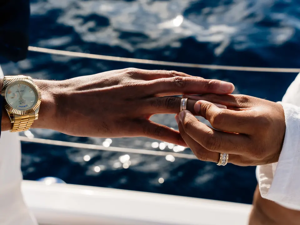 Close-up of an engagement ring being placed on a bride-to-be's finger above the blue Aegean Sea