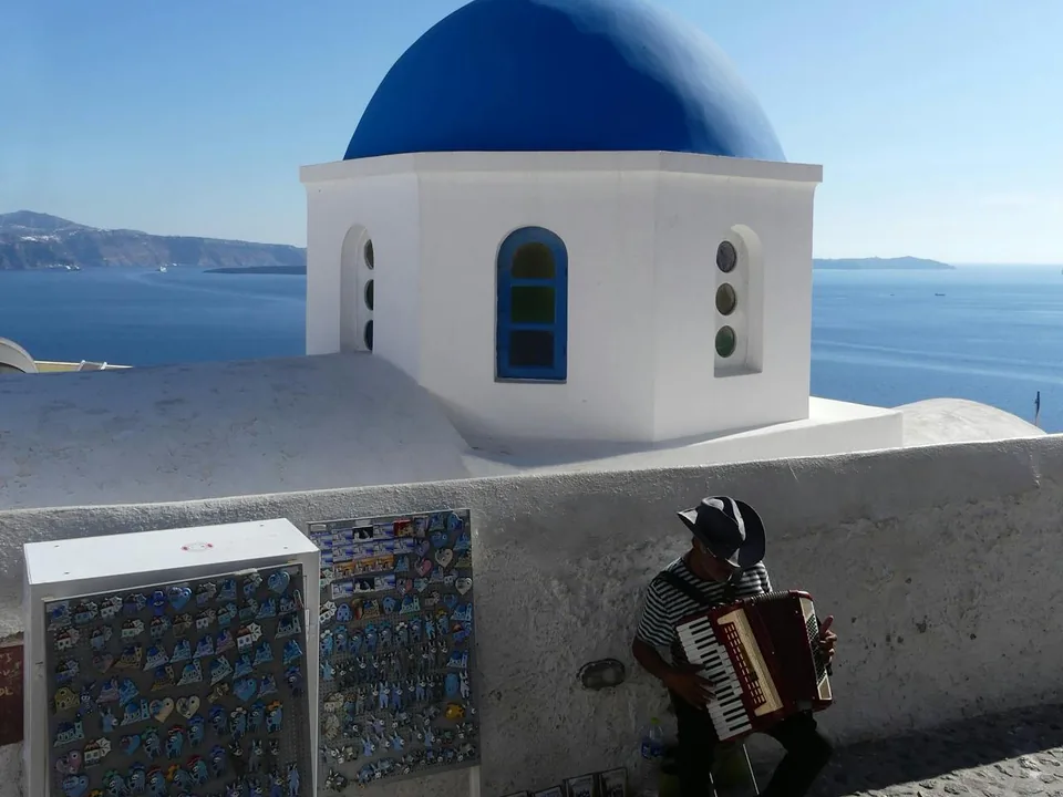 A musician playing live by an iconic blue-domed church above the Santorini caldera